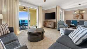 A spacious living area with a large round coffee table, comfortable seating, a ceiling fan, a flat-screen TV, and a view to the outside. - Penthouse Premium 3BR Condo - 1900+ Sq Ft - Beach Service Included (Panama City Beach)