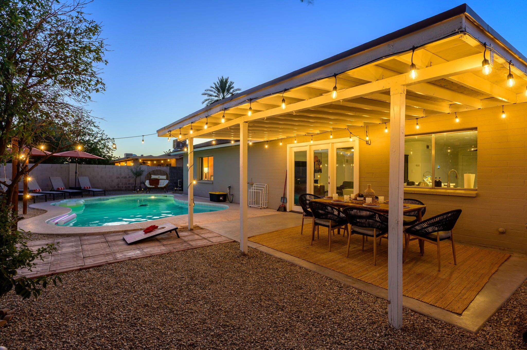 A covered outdoor patio with a pool, lounge chairs, and a dining area.