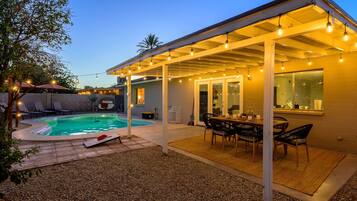A covered outdoor patio with a pool, lounge chairs, and a dining area.
