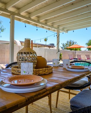 An outdoor patio with a wooden table set for dining, featuring woven baskets, plates, and a decorative vase. - Stylish Phoenix home | Private pool | Spacious living | Family & sports-friendly | Close to Phoenix Zoo, Desert Botanical Garden, ASU, and State Farm Stadium (Phoenix)
