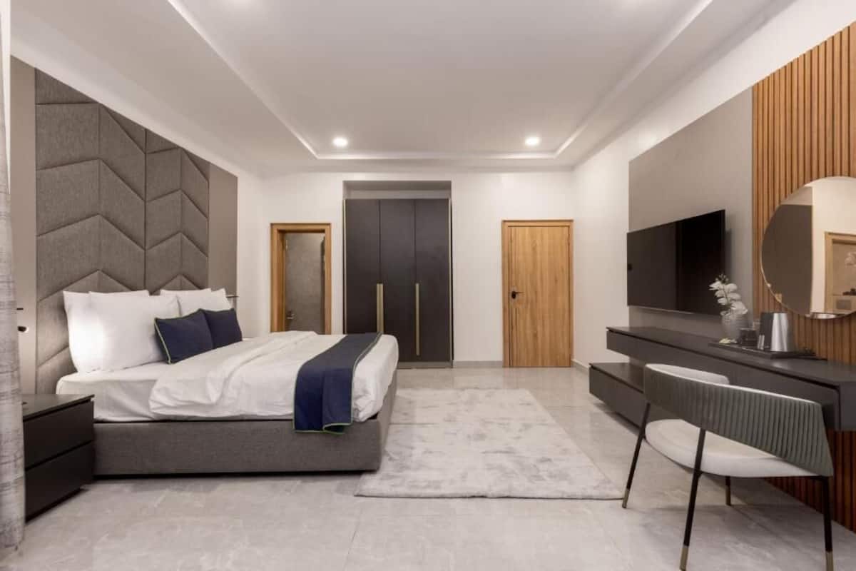 A modern bedroom with a bed, bedside tables, a vanity with a mirror, and a television.