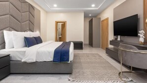 A modern bedroom with a large bed, a TV, and a minimalist design. - STP Apartments (Abuja)