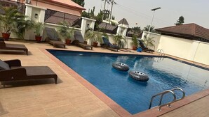 A swimming pool with lounge chairs and potted plants. - STP Apartments (Abuja)