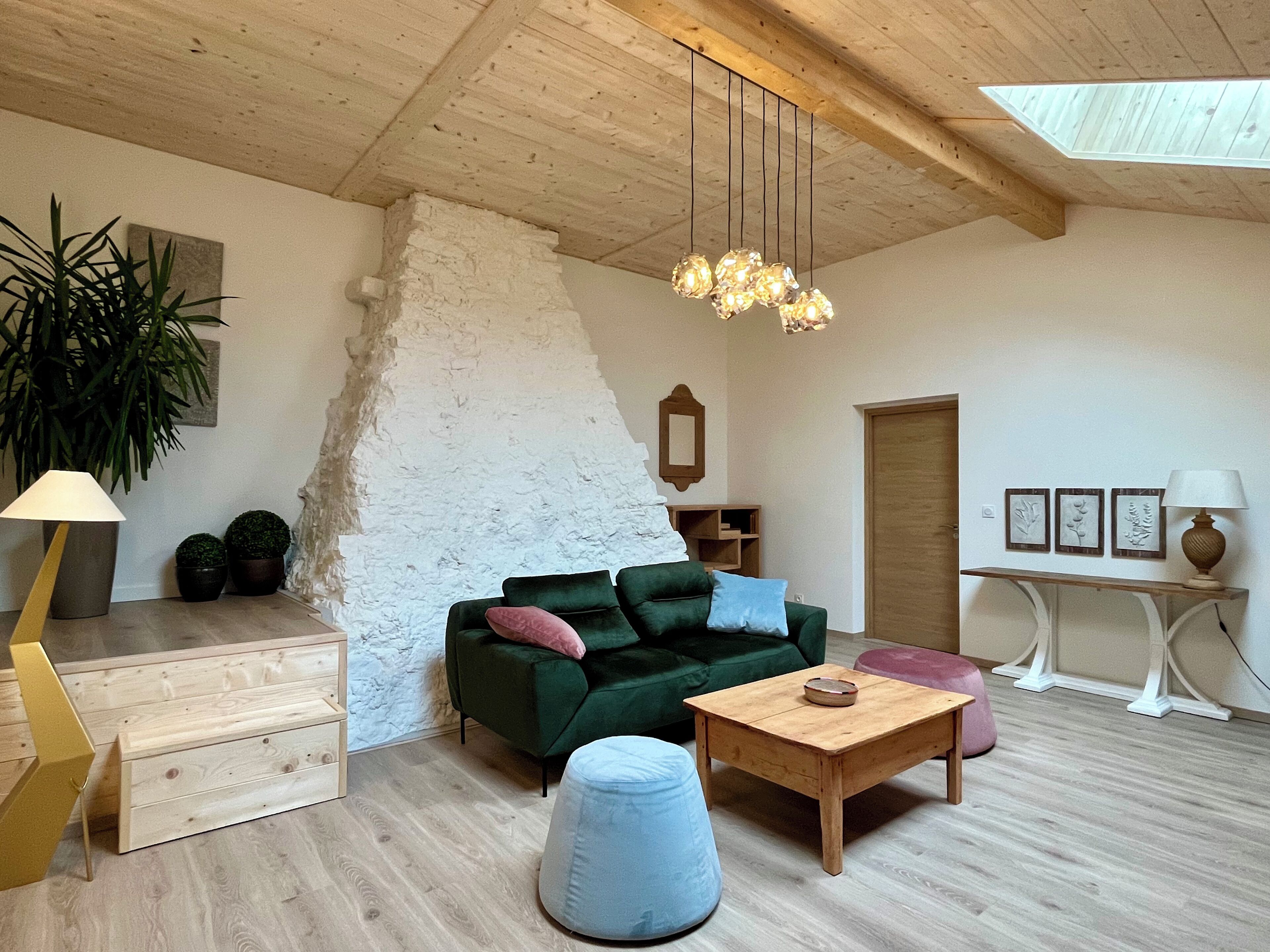 A spacious living room with a wooden ceiling, a green sofa, a wooden coffee table, a blue ottoman, and a wooden cabinet.