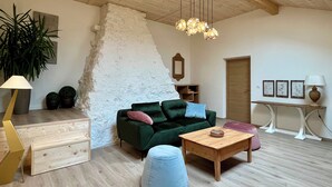 Un salon spacieux avec un plafond en bois, un canapé vert, une table basse en bois, un pouf bleu et un meuble en bois.