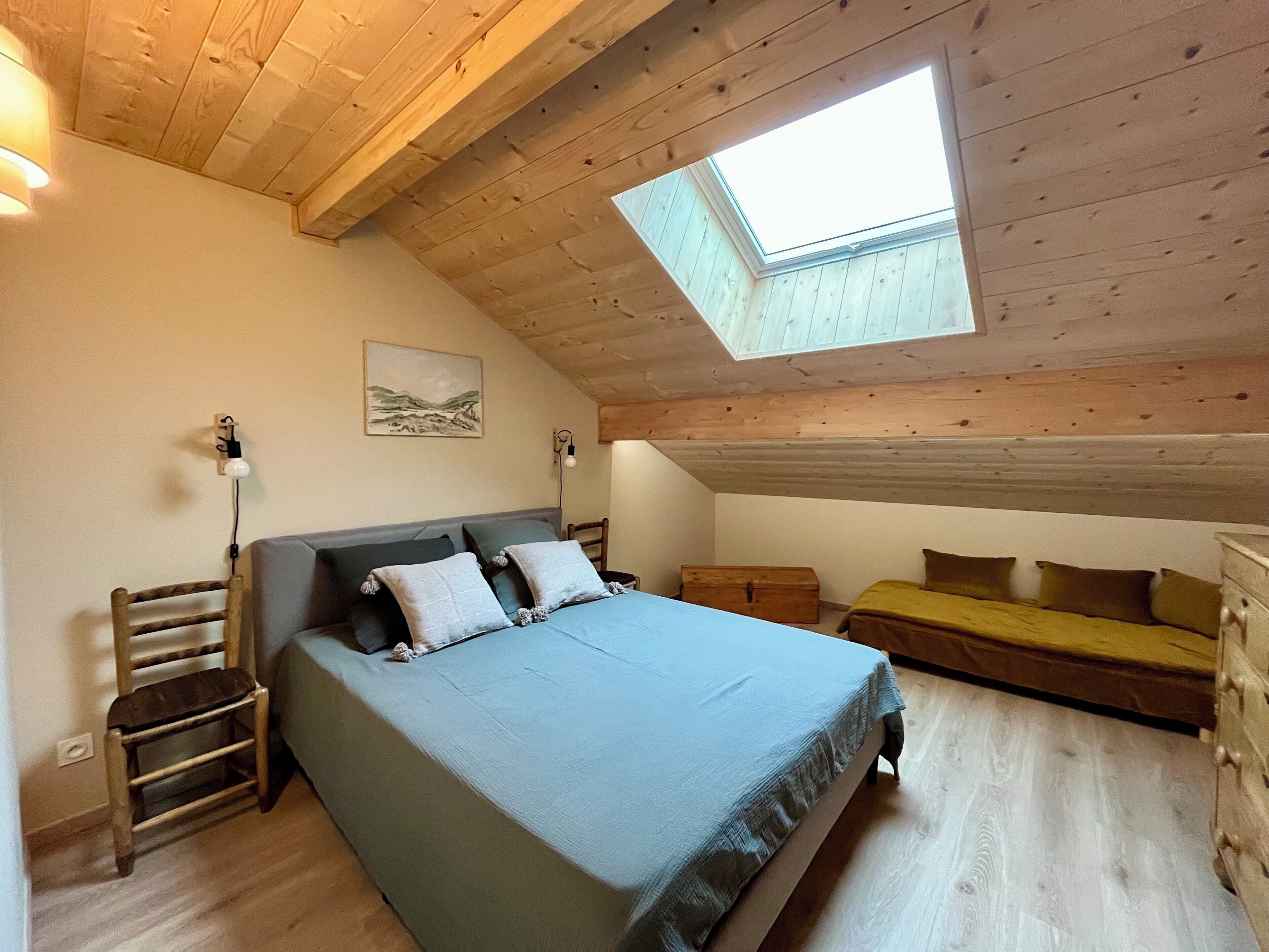 Ein Schlafzimmer mit Oberlicht, einem Bett, einer Bank und einer Kommode.