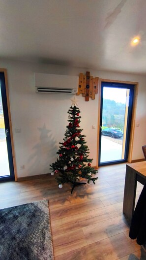 Ein modernes Wohnzimmer mit geschmücktem Weihnachtsbaum, einer hölzernen Wanduhr und Blick durch ein großes Fenster.