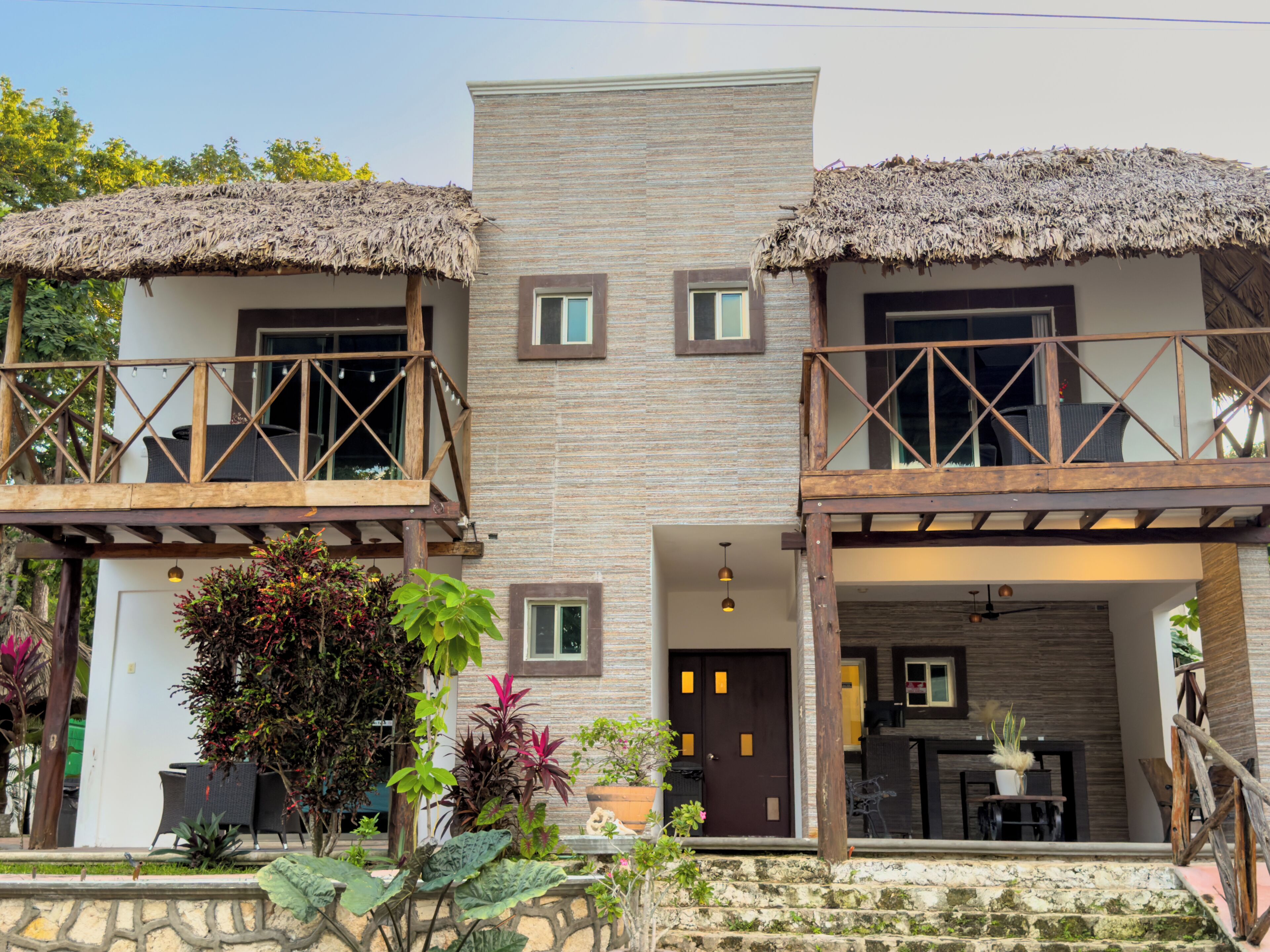 A two-story building with a balcony on each floor, a stone staircase, and a small garden area.