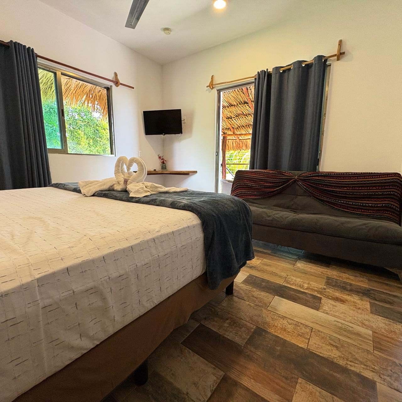 Habitación de hotel con cama, sofá, televisor de pantalla plana y ventana con cortinas.