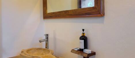 Un baño con un lavabo de madera, un espejo y una estantería con una botella y una caja.