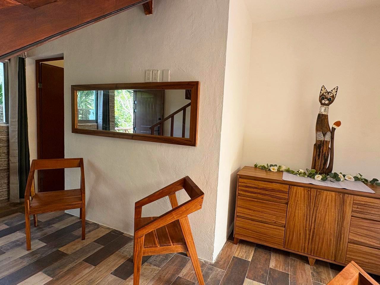 Una habitación con suelo de diseño espiga, un banco de madera, un espejo y un aparador con una figurita de gato.