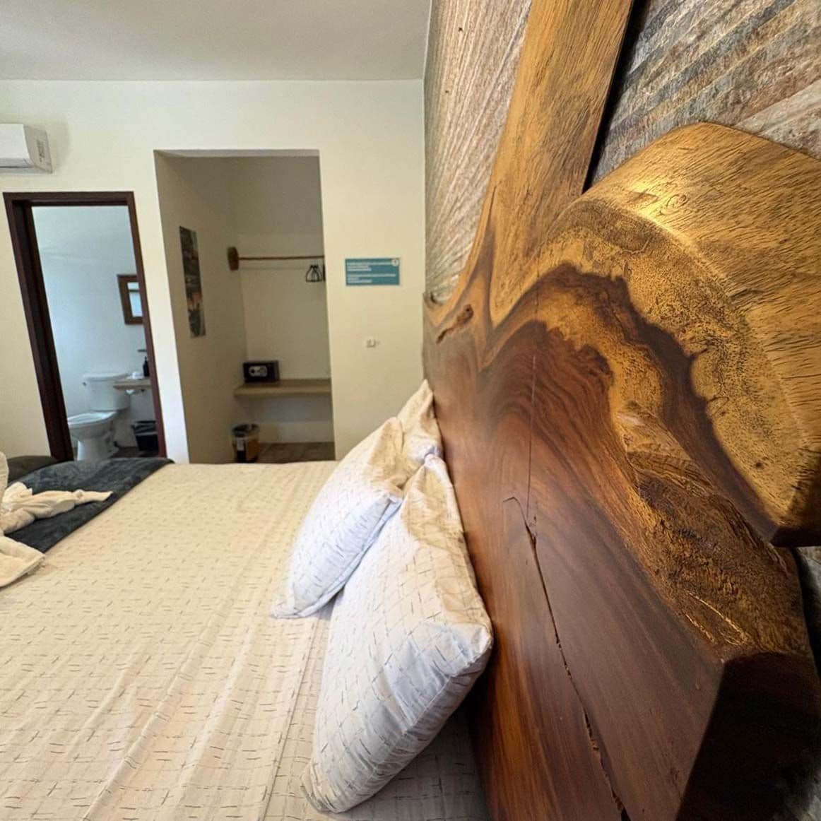 A bedroom with a wooden headboard, a bed with a patterned bedspread, and a visible bathroom in the background.