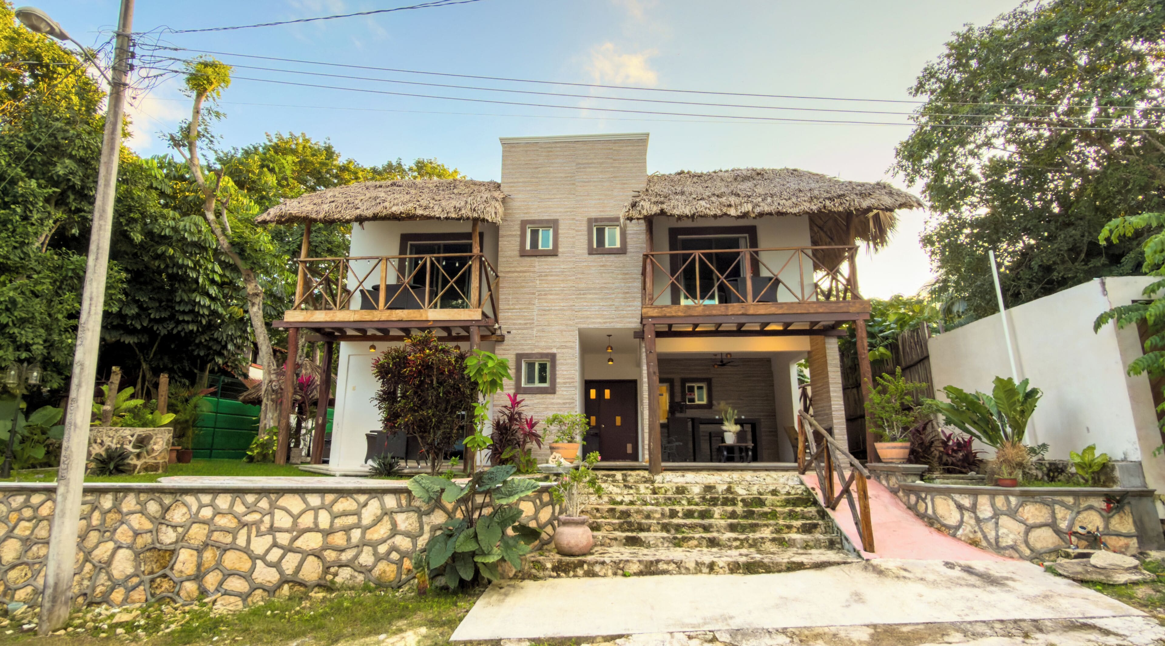 A two-story house with a stone facade, a thatched roof, and a staircase leading to the entrance.