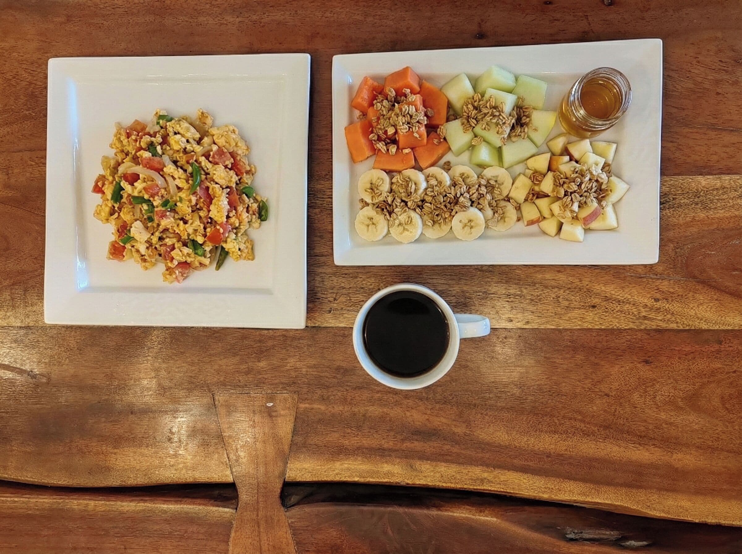 Two white plates of food and a cup of black coffee on a wooden table.