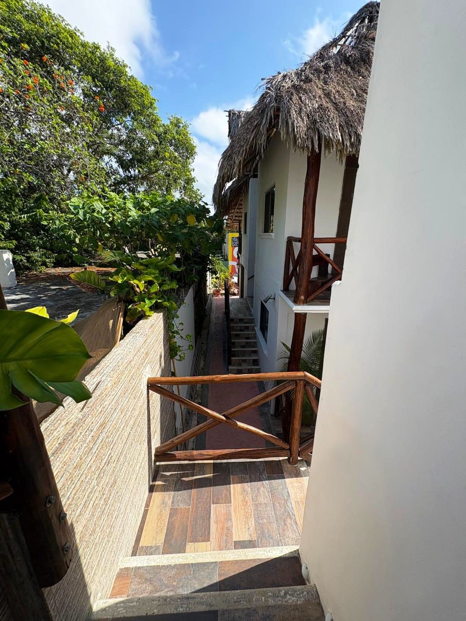 A staircase leading to a building with a thatched roof, surrounded by greenery.