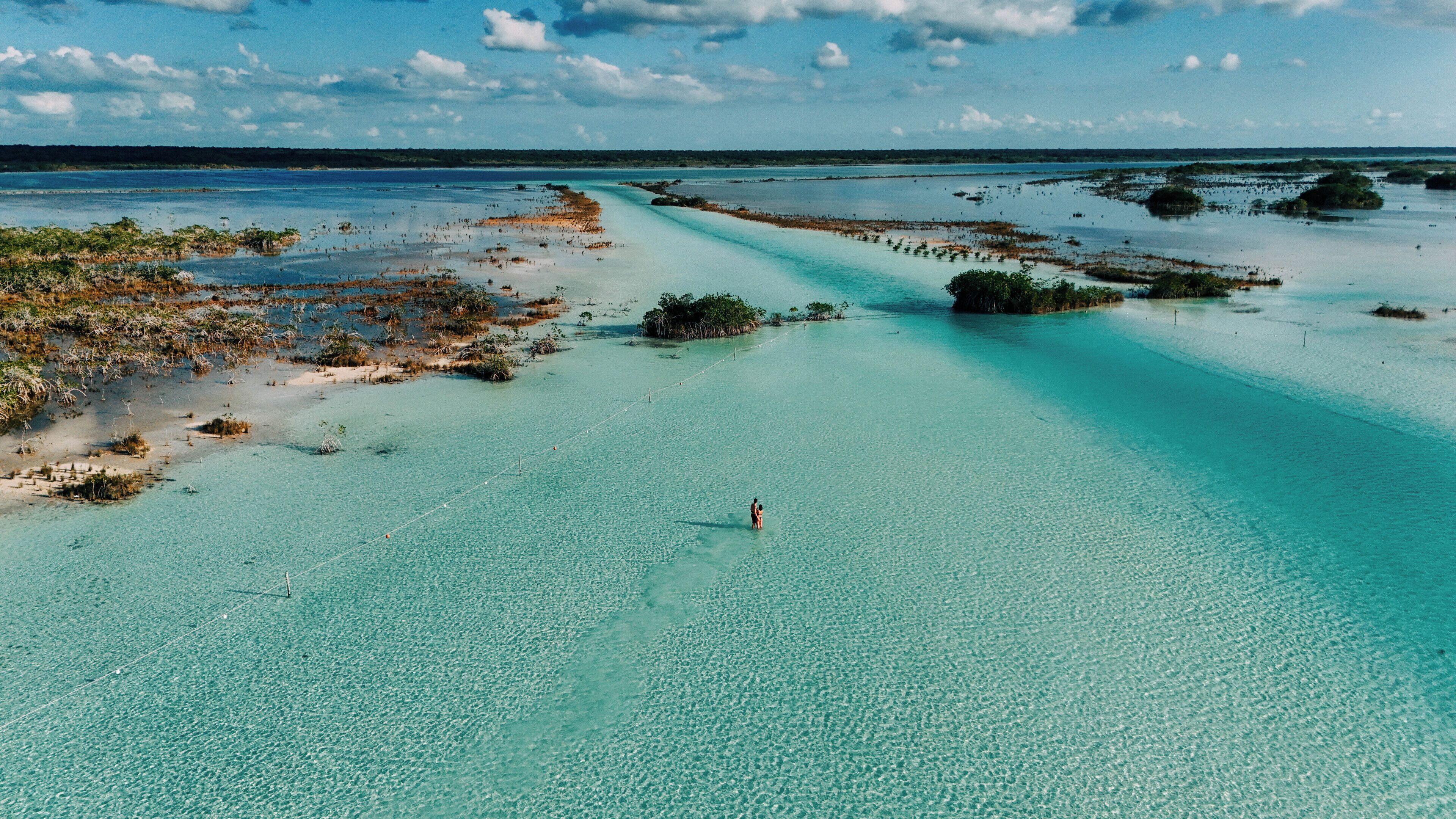 Paesaggio costiero con acque cristalline color turchese, una persona in acqua e una costa lontana con vegetazione.