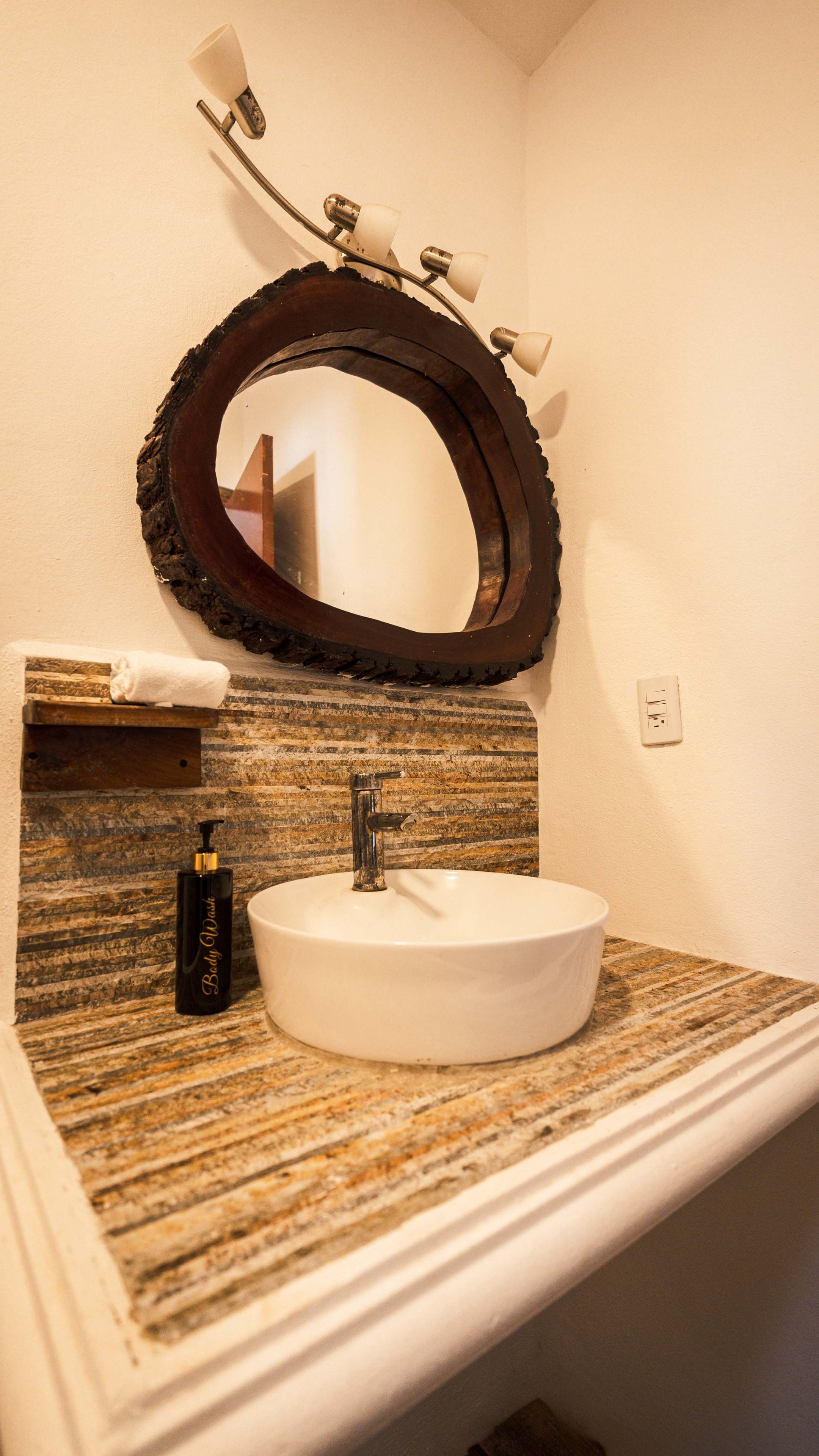 A bathroom with a round mirror, a white sink, and a soap dispenser.