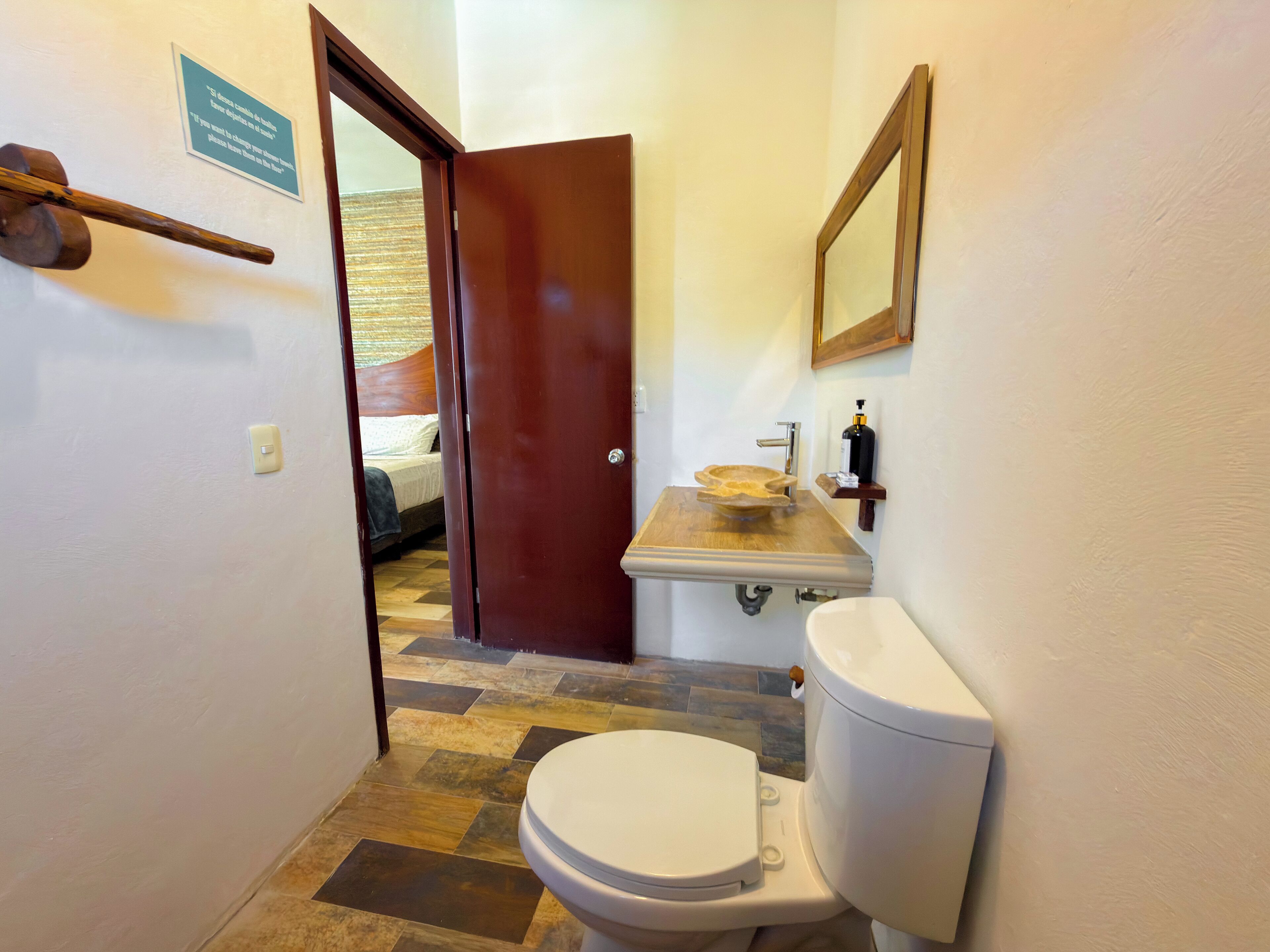 A bathroom with a toilet, sink, and a wooden door leading to a bedroom.