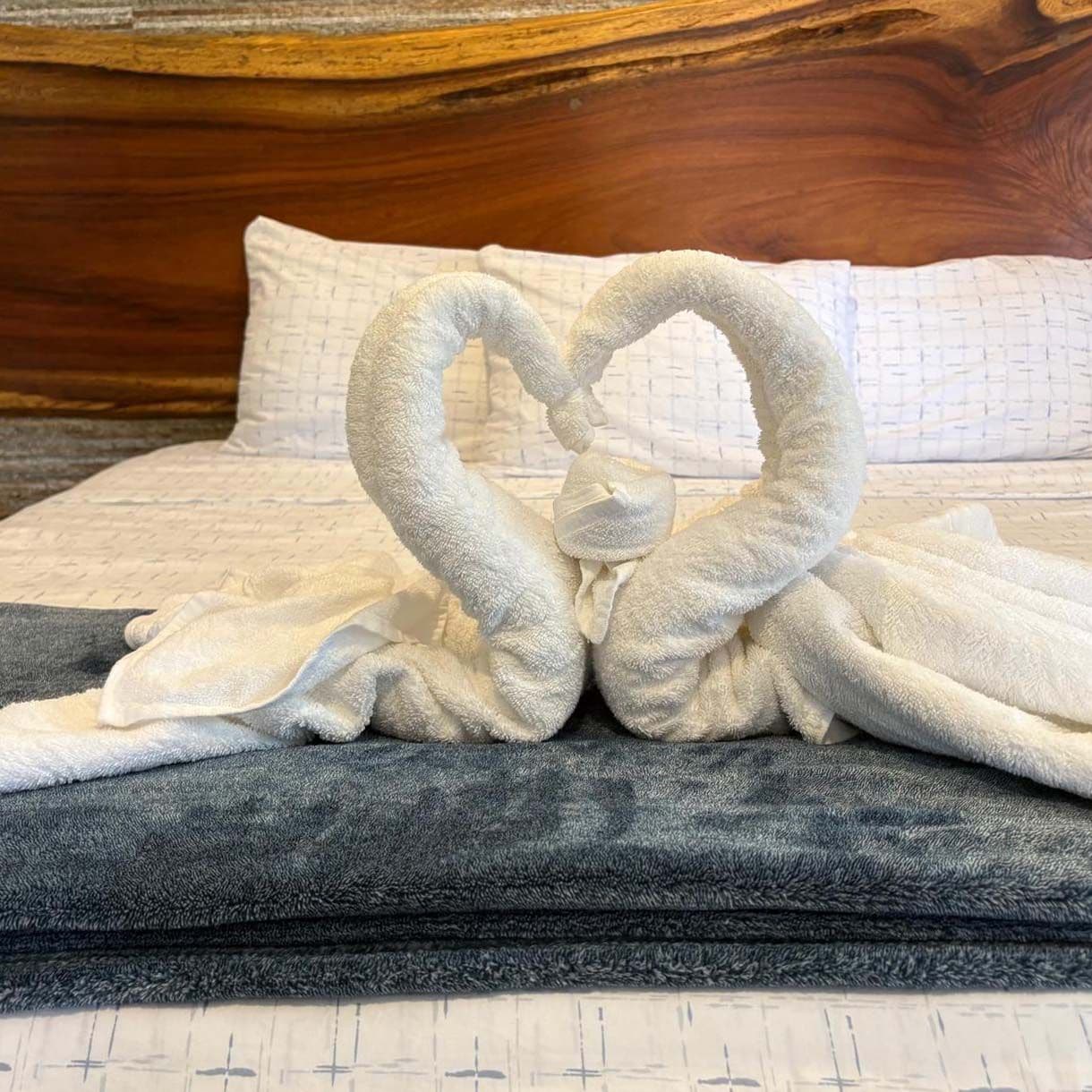 Una cama con cabecera de madera, colcha estampada y manta gris oscuro.