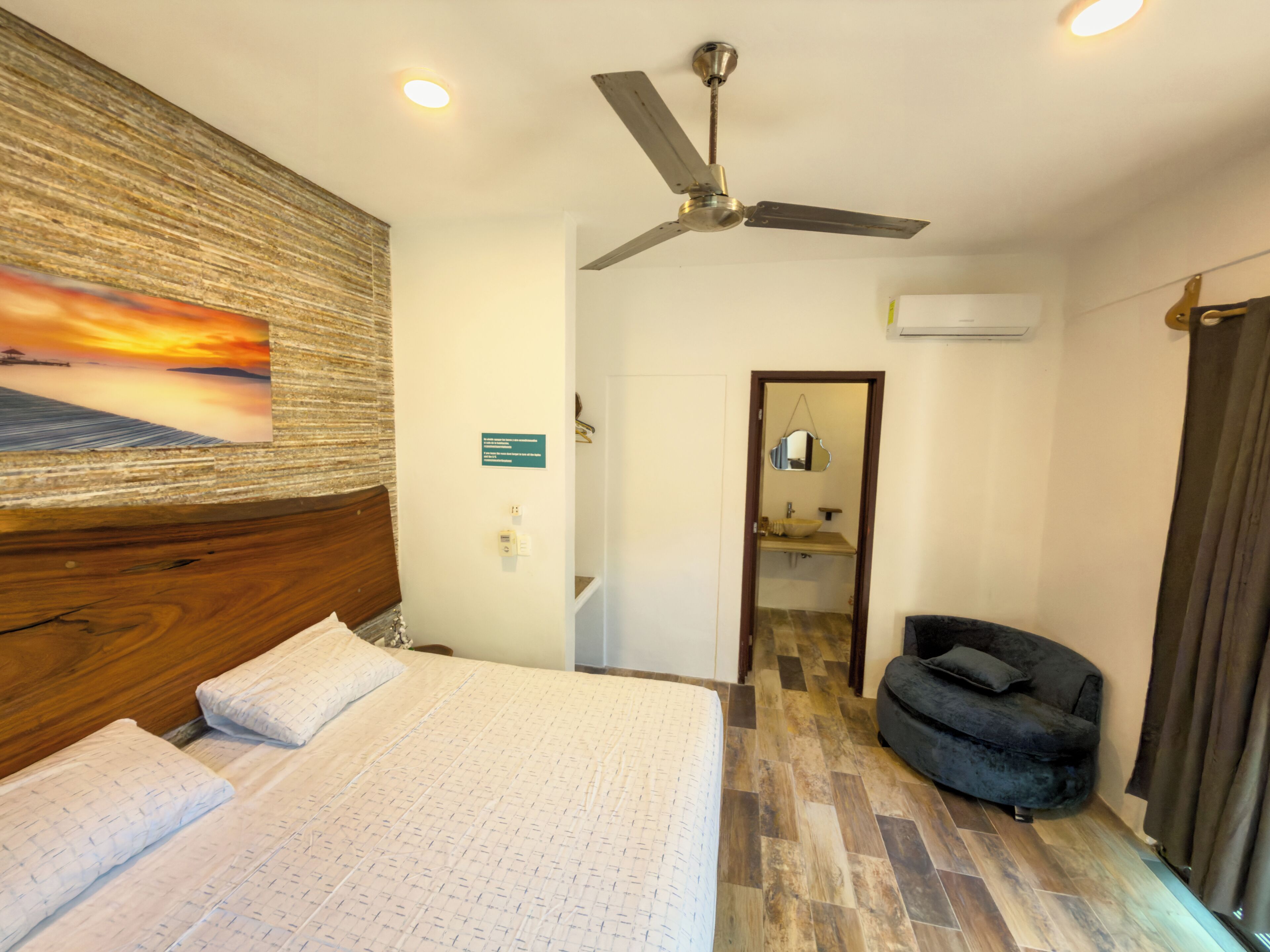 A hotel room with a bed, a ceiling fan, a bathroom with a sink and mirror, and a chair.