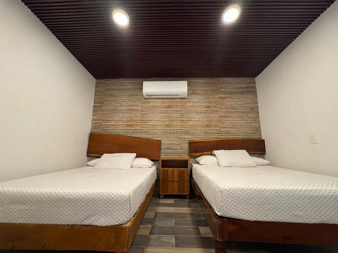Quarto com duas camas de madeira, ar-condicionado fixado na parede e piso de azulejos.