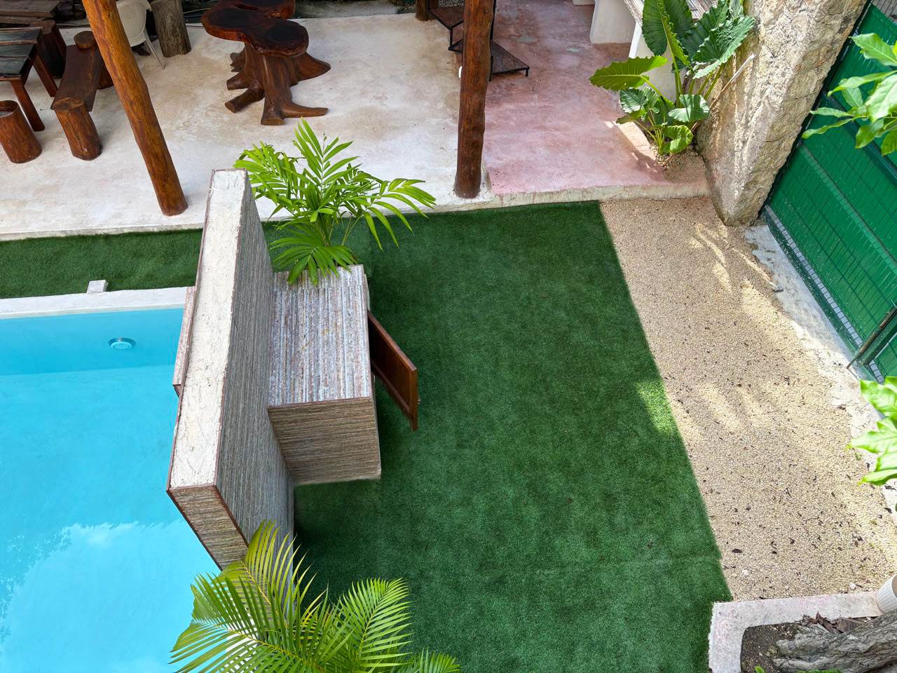 Area piscina con prato sintetico, fioriera in cemento e mobili in legno.