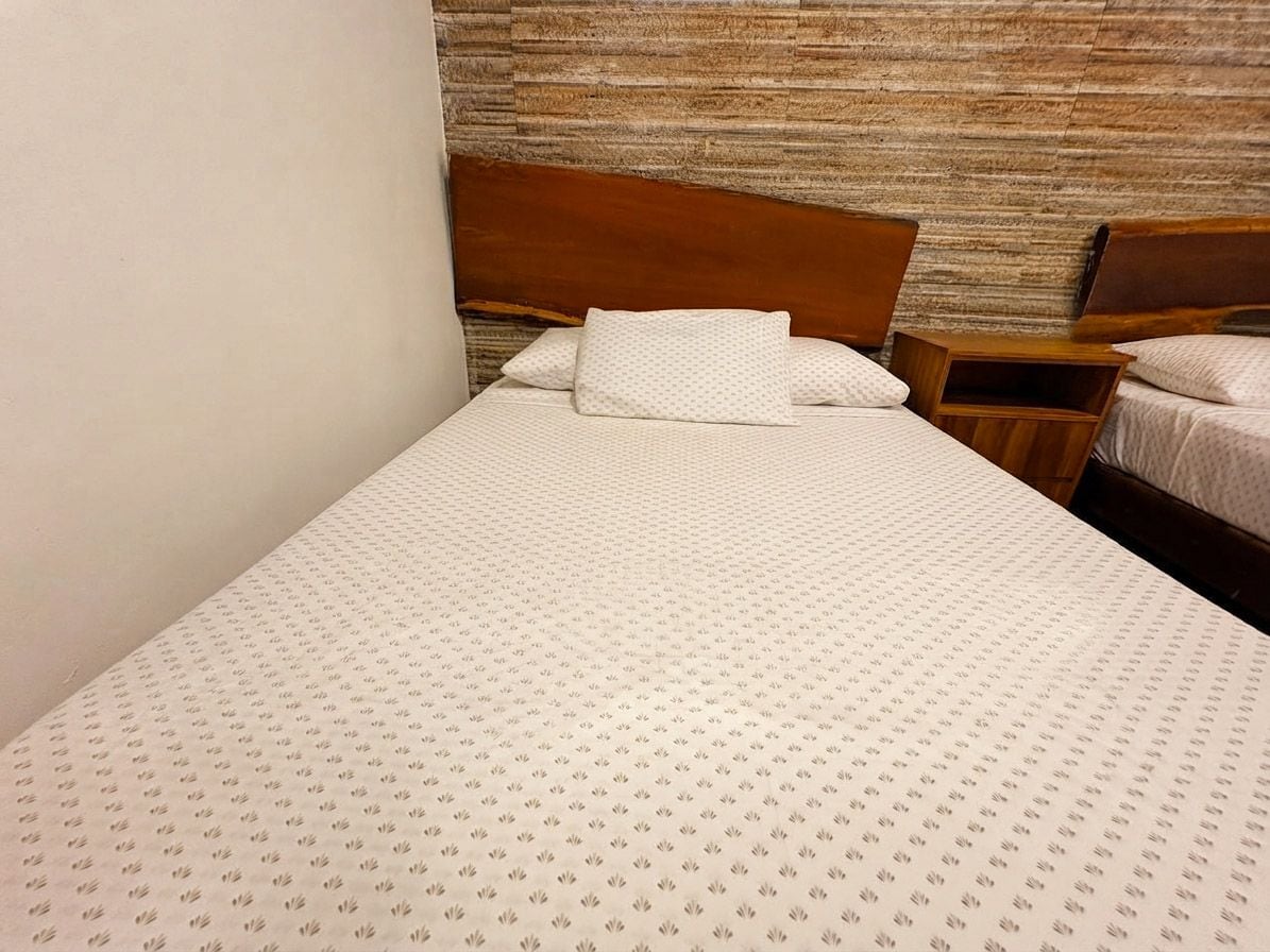 Un lit simple avec une couvre-lit à motifs, une tête de lit en bois et un mur texturé en arrière-plan.