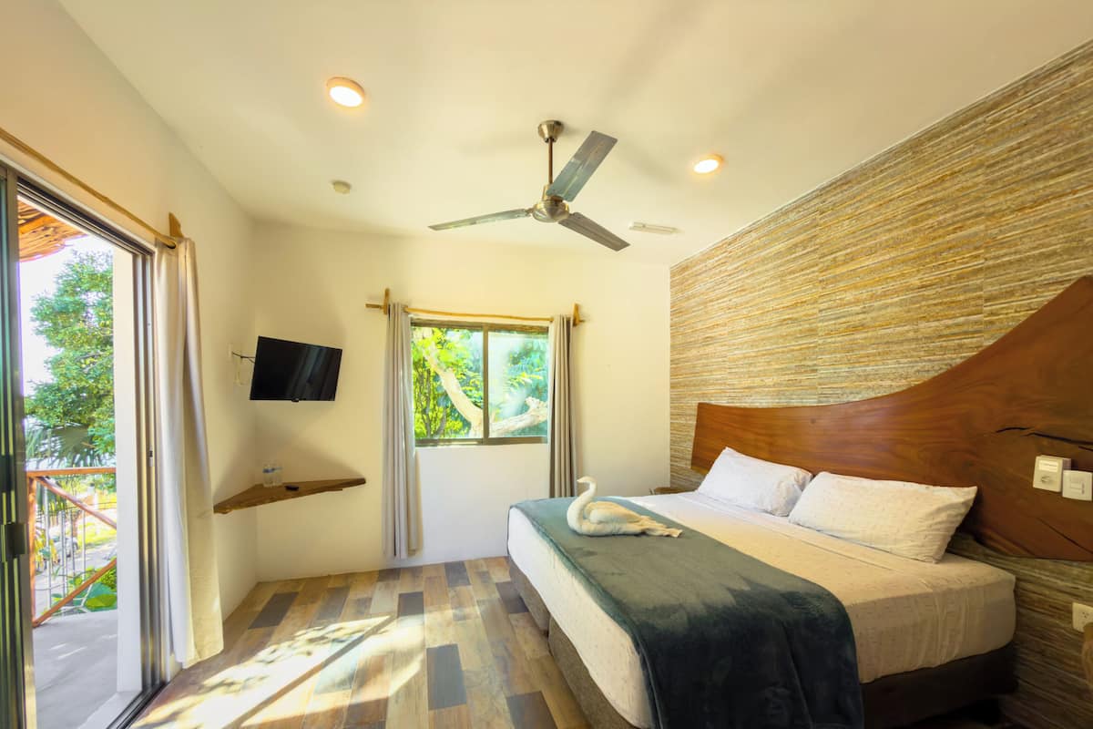 A bedroom with a bed, a ceiling fan, a TV, and a window with curtains.