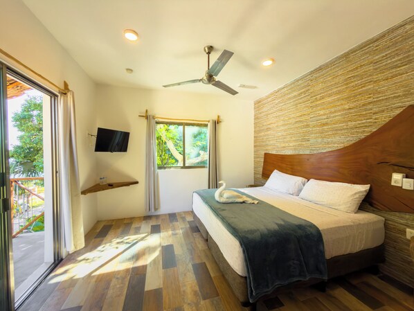 A bedroom with a bed, a ceiling fan, a TV, and a window with curtains.