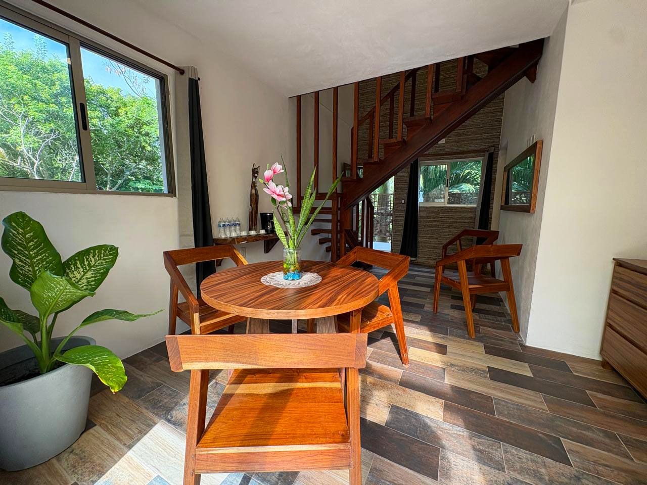 A dining area with a round wooden table and chairs, a potted plant, and a staircase leading to an upper level.