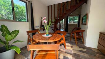 A dining area with a round wooden table and chairs, a potted plant, and a staircase leading to an upper level.