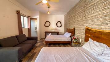 A bedroom with a bed, a wooden headboard, a nightstand, a small table with a vase of flowers, a ceiling fan, and a wall-mounted air conditioner.