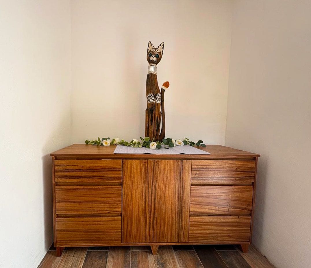 A wooden cabinet with drawers and a decorative cat figurine on top.
