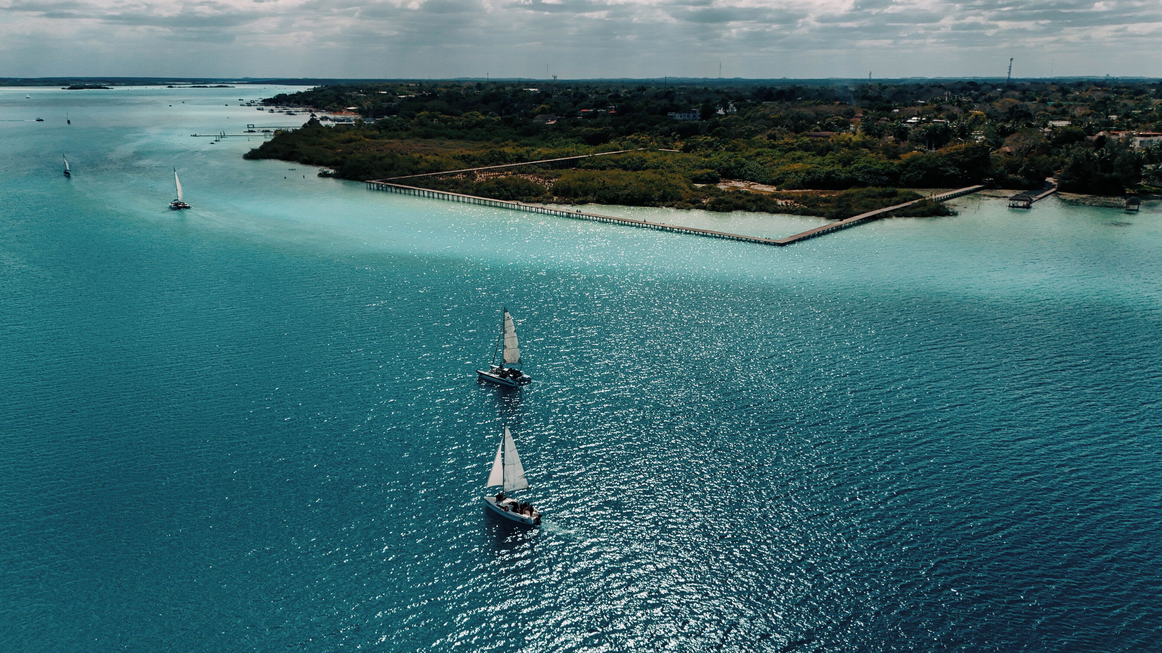 Zona costera con muelle que se adentra en el agua, barcos y una orilla distante con vegetación.