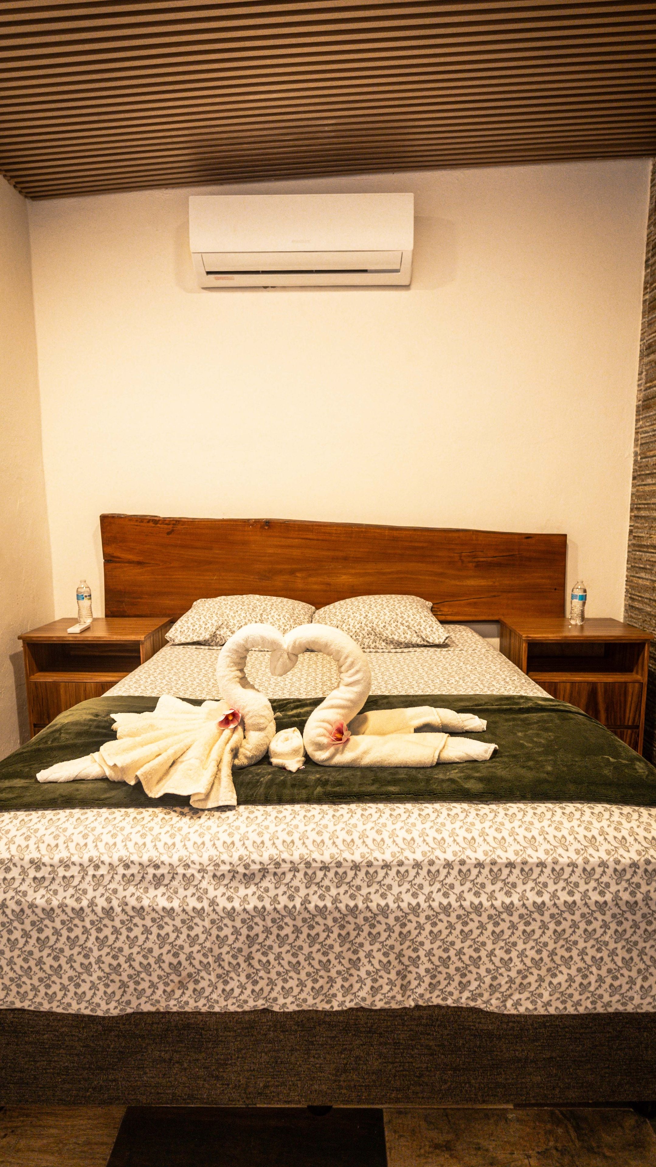 A hotel room with a bed, two nightstands, a water bottle on each, and a heart-shaped towel arrangement.