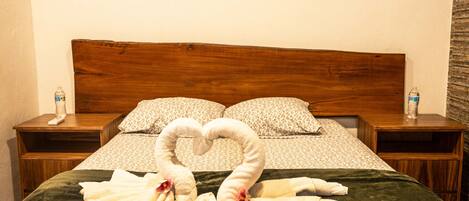 A hotel room with a bed, two nightstands, a water bottle on each, and a heart-shaped towel arrangement.