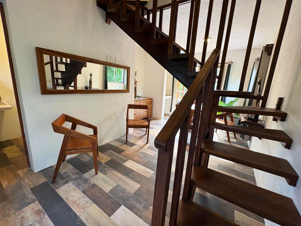 A staircase with wooden railings, a wooden chair, and a mirror on the wall.