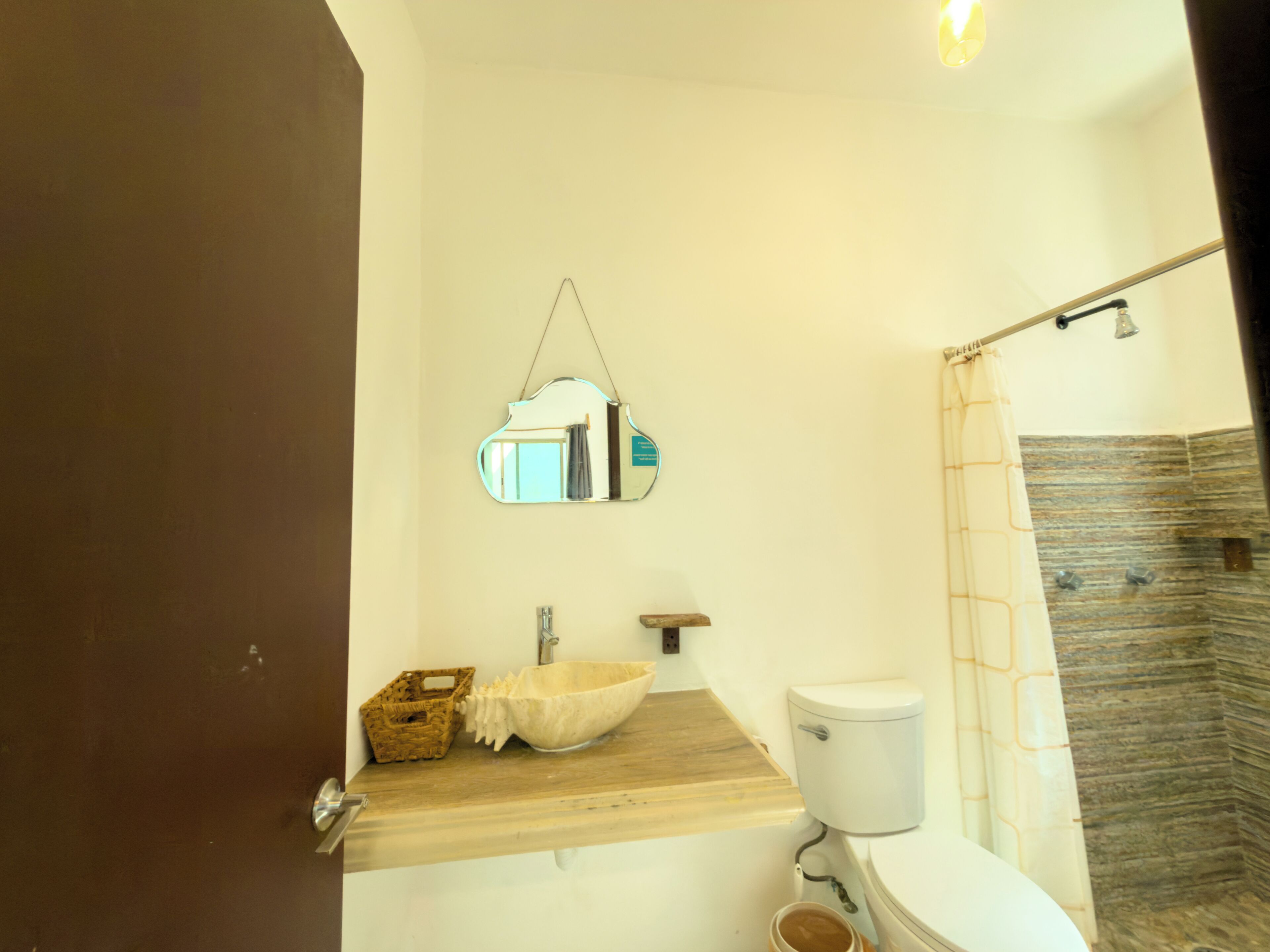 A bathroom with a wooden vanity, a white sink, a toilet, a hanging mirror, and a shower curtain.
