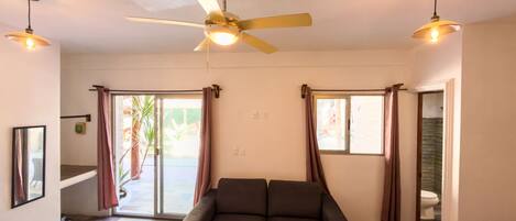A spacious room with a dark sofa, a ceiling fan, and two pendant lights.