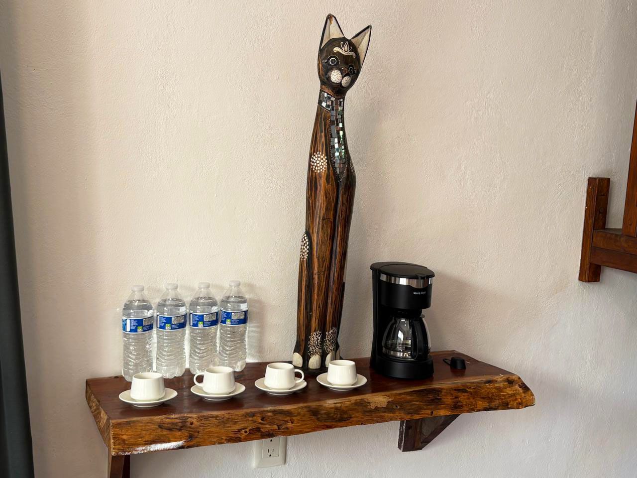 A wooden shelf with water bottles, coffee maker, and a decorative cat figure.