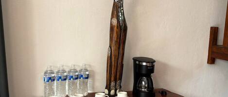 A wooden shelf with water bottles, coffee maker, and a decorative cat figure.