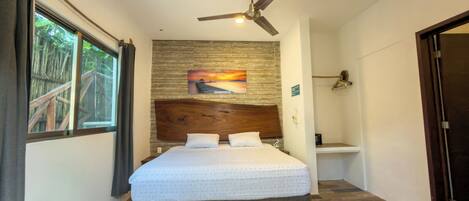 A bedroom with a large bed, a ceiling fan, a painting on the wall, and a window with curtains.