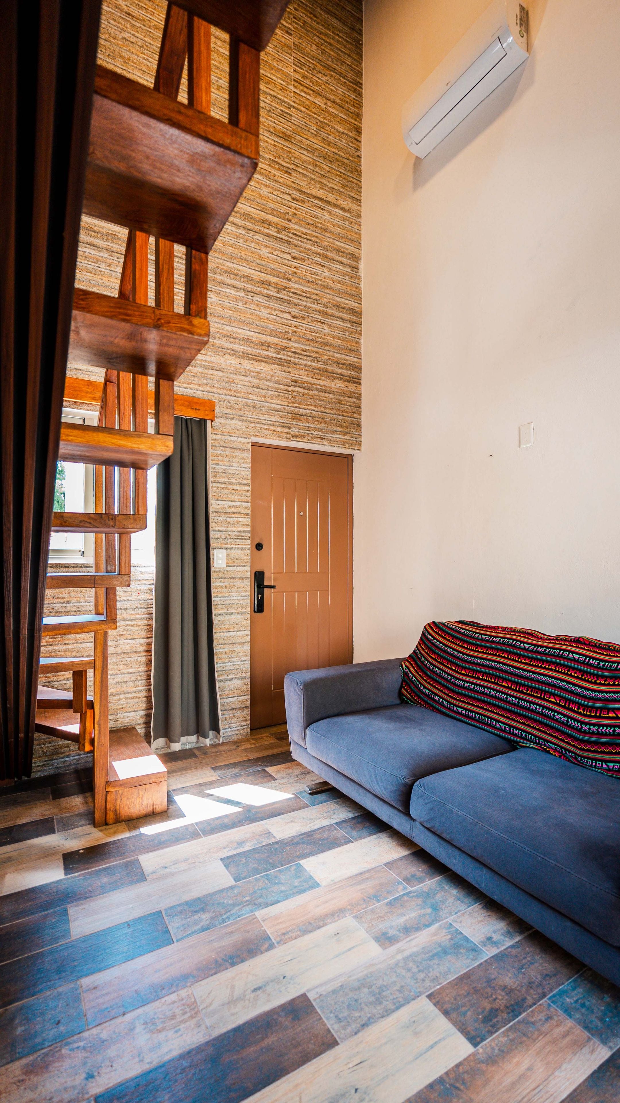 Quarto com escada de madeira, um sofá e um cobertor estampado.