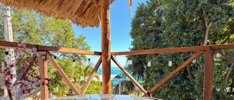 A glass-top table with a woven wicker frame, supported by wooden beams, under a thatched roof structure.