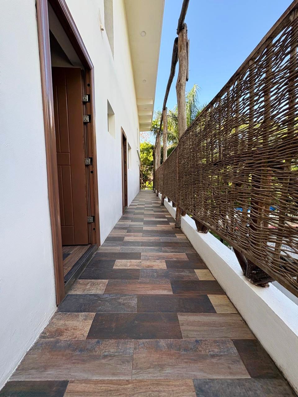 A corridor with a checkered floor, a wooden door, and a woven fence.