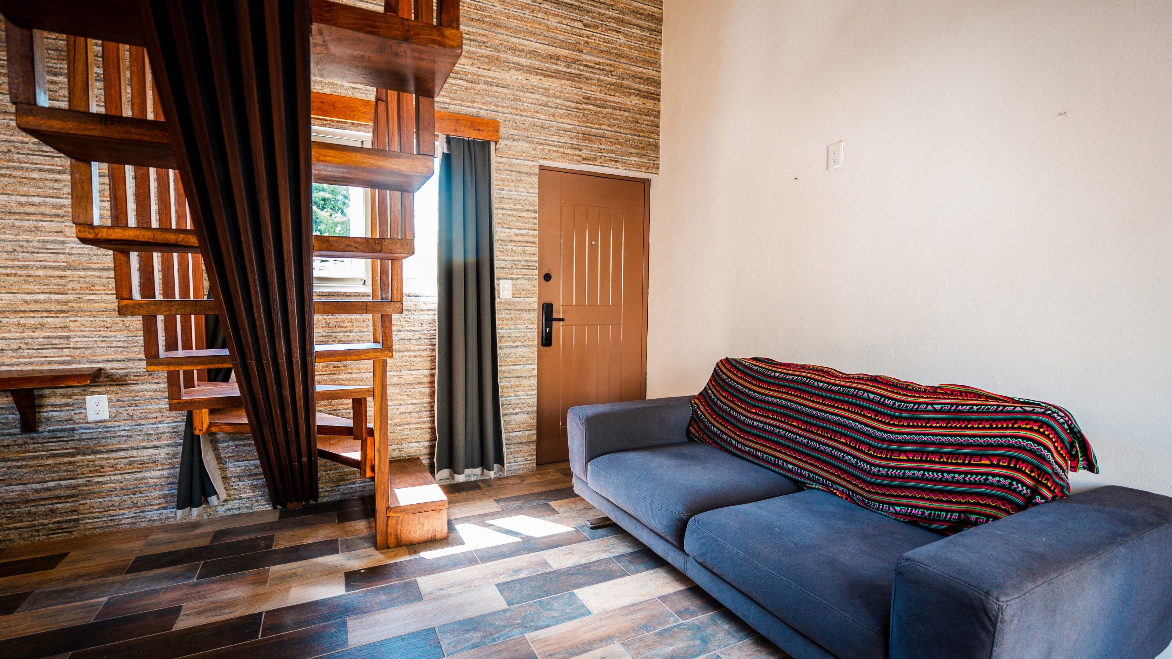 Quarto com um sofá azul, escada de madeira e um cobertor estampado no sofá.