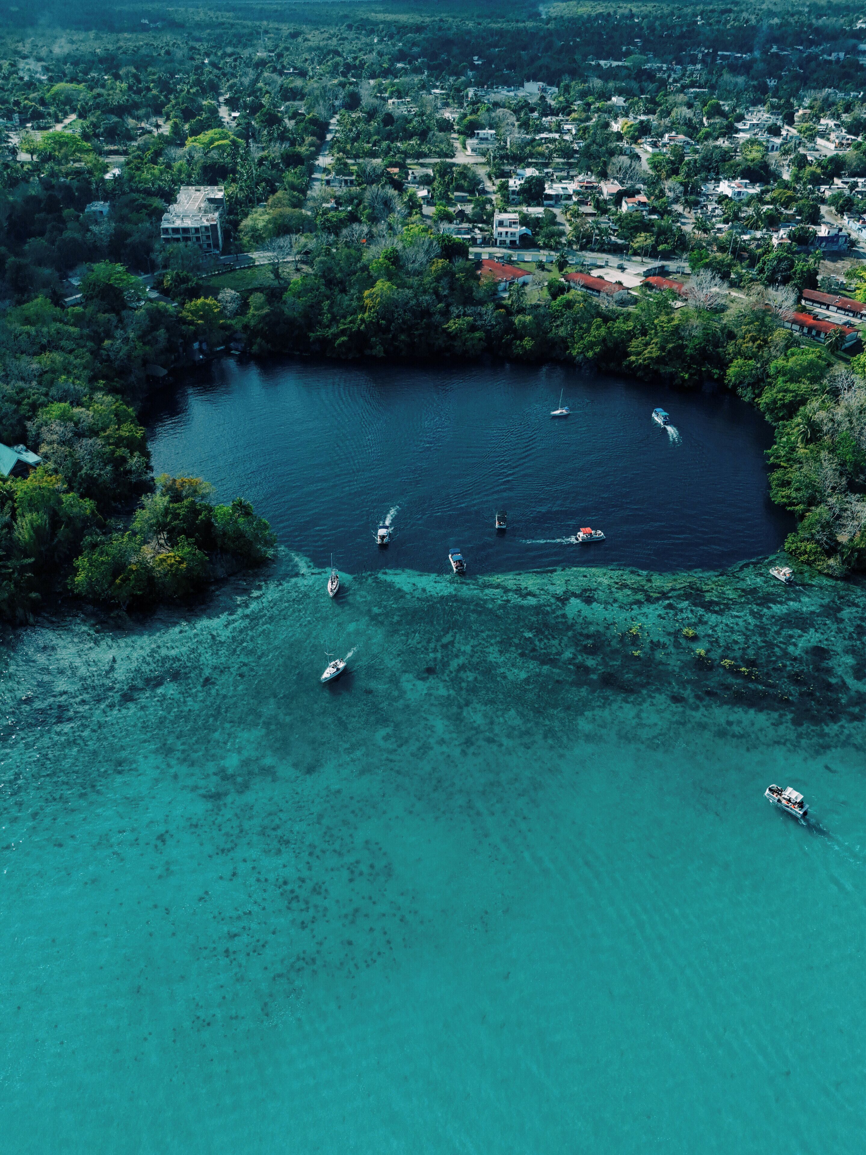 An aerial view of a coastal town with clear turquoise waters, boats, and dense greenery.