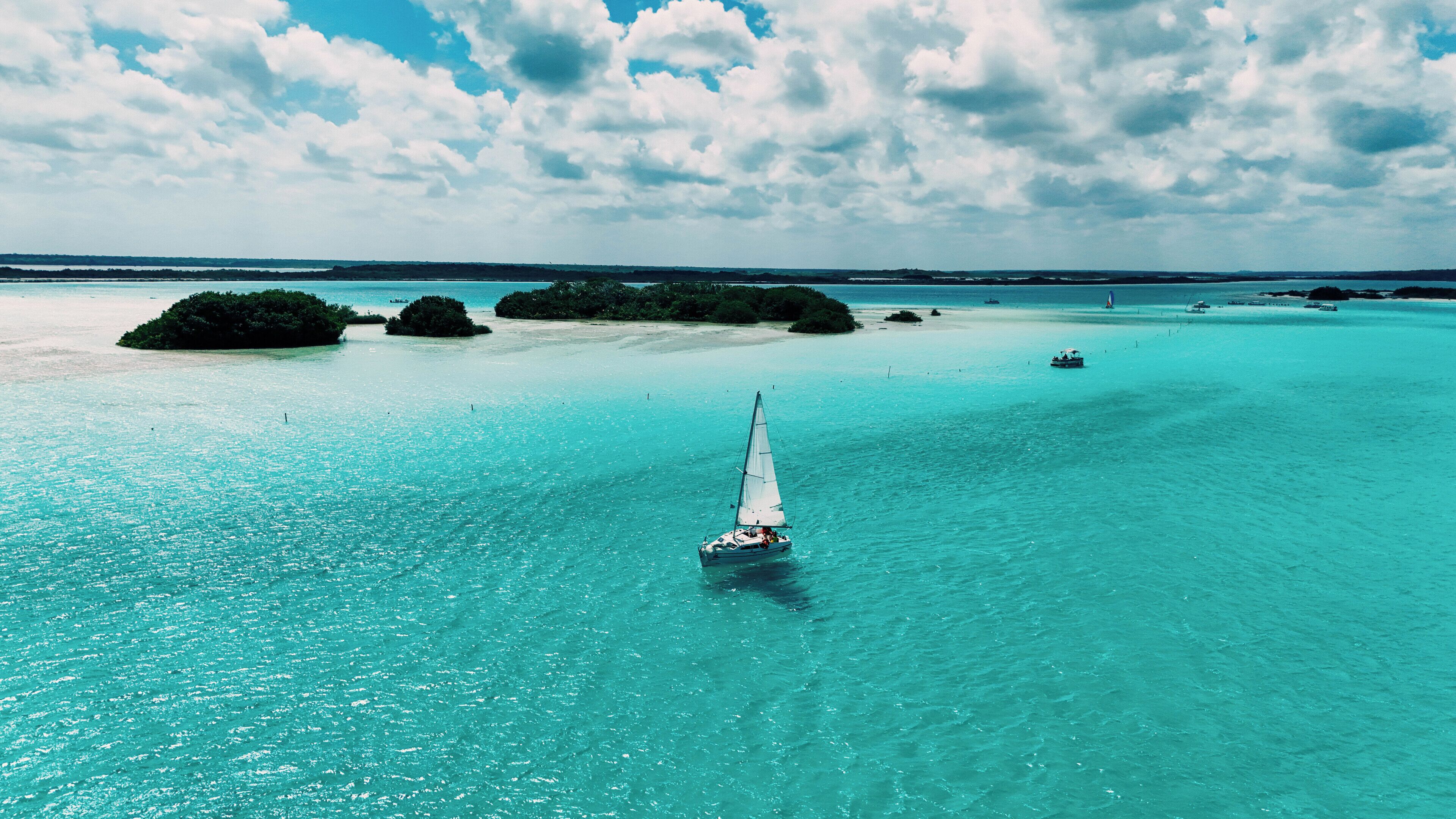 Un voilier sur des eaux turquoise, avec des îles lointaines et un ciel dégagé.