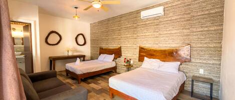 A hotel room with two beds, a wooden headboard, a ceiling fan, a small table, and a couch.