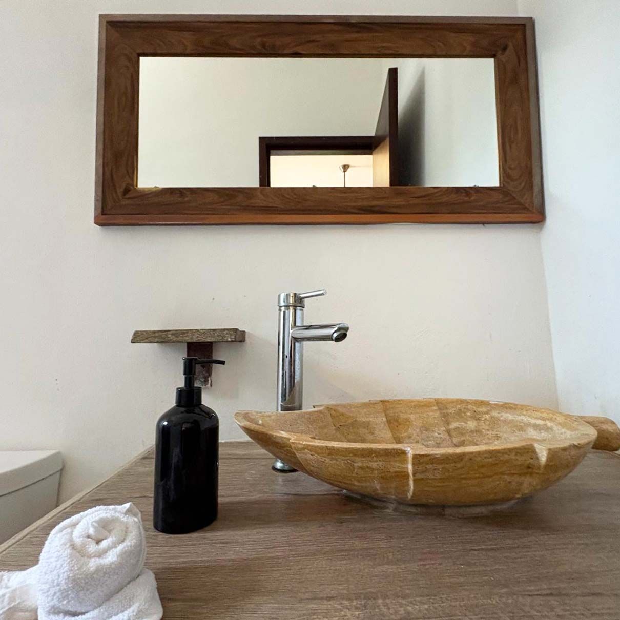 A bathroom with a wooden bowl sink, a black soap dispenser, and a mirror above the sink.